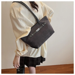Dark gray suede tote bag with buckle strap detail worn by a model in casual style