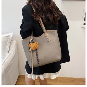 Detail of taupe pebbled leather tote bag with gold lettering and plush bear charm