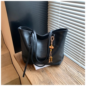 Dettaglio borsa shopper nera con manici lunghi e nappa etnica con perline su base in legno