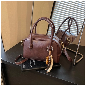 Detail of dark brown boston bag with lychee grain texture and multi-colored wood bead charm
