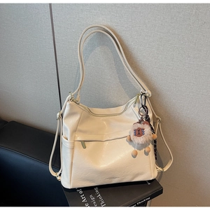 Detail of cream shoulder bag with plush bear charm and adjustable crossbody strap