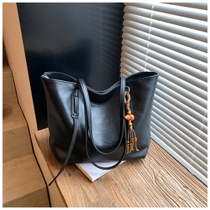 Dettaglio della borsa tote nera con nappina in perle di legno su trama in pelle