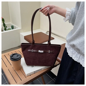 Detail of a dark brown suede bucket bag with metal buckle on a wooden desk setup