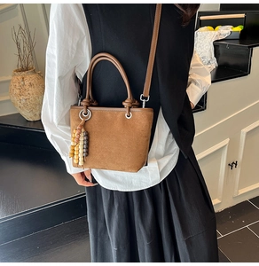 Detail view of brown suede bucket bag featuring chic beaded charm and metal handle ring