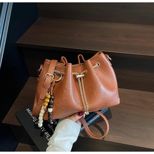 Detail view of brown leather bucket bag with chain drawstring and beaded pendant on stairs