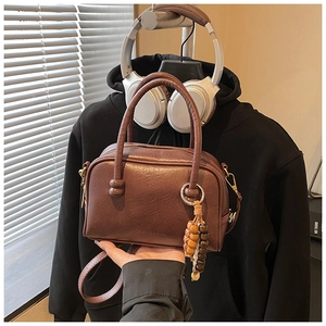 Detail of a brown Boston style handbag featuring lychee texture and wooden bead charm