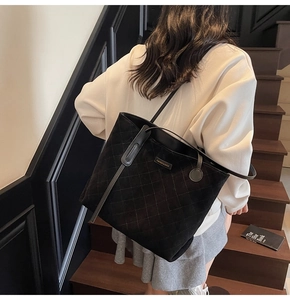 Detail of black quilted suede tote bag featuring fashion metal logo and long shoulder strap
