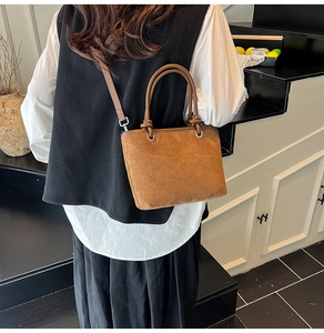 Detail of caramel brown suede handbag showing knot handle and silver metal hooks