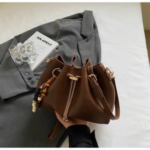 Detail view of dark brown drawstring bucket bag with beads charm and chain