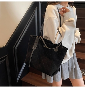Detail of black suede tote bag featuring quilted rhombus pattern and fashion label