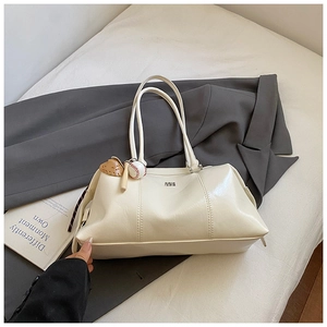 Close-up of cream shoulder bag with shiny finish, metal logo and baseball charm detail