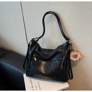 Detail of a large black soft leather tote bag with a camel alpaca plush charm accessory