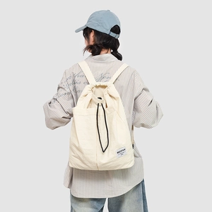 Detail of cream drawstring backpack showing side pocket and nylon fabric texture