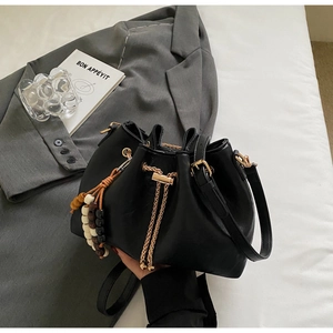 Detail of black faux leather bucket bag with gold chain drawstring and beaded pendant charm