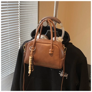 Detail of a brown leather bowling bag with wooden bead charm and metal hardware