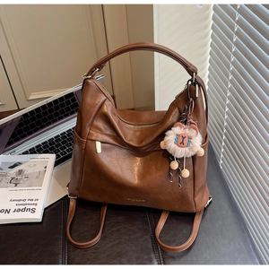 Detail view of brown matte leather shoulder bag featuring adjustable straps and plush charm