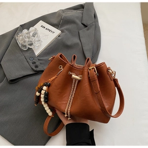 Detailed shot of brown bucket bag with golden chain drawstring and beaded pendant charm