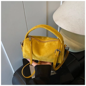 Nahaufnahme einer gelben Wildleder-Zylindertasche mit silbernen Metallteilen und Henkel