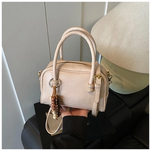 Detail of beige bowling bag with textured leather, beaded charm and top handles
