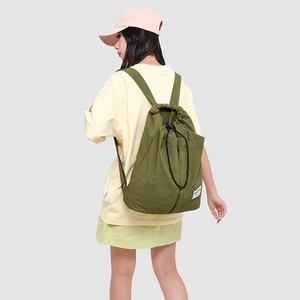 Army green nylon drawstring backpack with side logo label worn by model outdoors