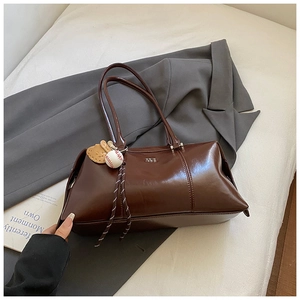 Detail of dark brown glossy leather bowling bag with baseball charm on a gray blazer