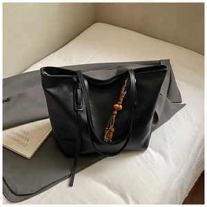 Dettaglio della borsa tote nera in pelle PU con nappa di perline su un blazer grigio