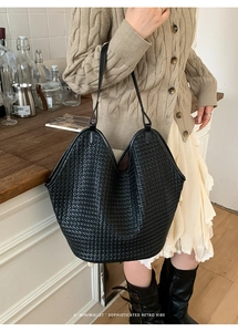 Detail view of black woven bucket bag with elegant minimalist retro texture and strap