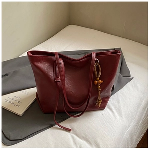 Dettaglio della borsa tote in pelle bordeaux con ciondolo in legno sopra un blazer
