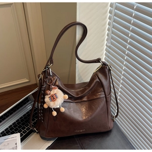 Close-up of coffee brown leather shoulder bag with cute plush bear charm in sunlight