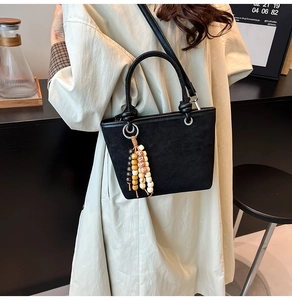 Detail of black suede bucket bag with wooden bead tassel charm on a beige trench coat