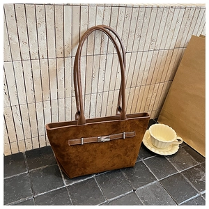 Detailed close-up of brown suede tote bag with metallic buckle in a minimalist setting