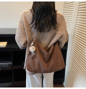 Sac hobo en daim marron avec breloque pelucheuse dans un décor de bibliothèque