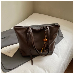 Dettaglio di una grande borsa tote marrone con trama martellata e ciondolo decorativo