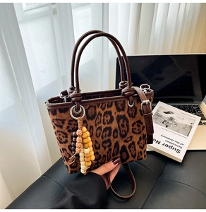 Detail of leopard print bucket bag with brown leather handle and wooden bead charm