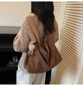 Détail du sac hobo en daim marron foncé avec charme en peluche porté par le mannequin
