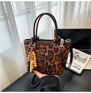 Leopard print bucket bag with brown leather handle and wooden bead detail on sofa