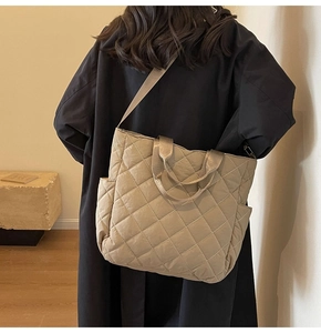 Detail of beige quilted tote bag with diamond pattern worn by a model in a black coat