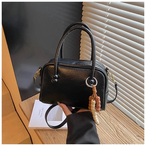 Detail of black bowling bag with golden hardware and fashion charm on a wooden desk