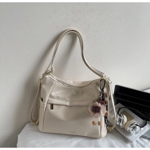 Detail of cream leather shoulder bag featuring a zipper and a plush lion charm