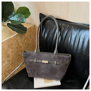 Detail of dark grey suede tote bag with metal buckle and long handles on a leather chair