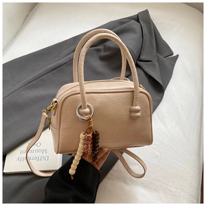 Detail of beige Boston handbag with beaded charm on a dark grey suit and white fabric