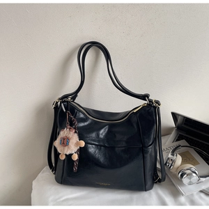 Detail of soft black leather tote with gold logo and plush sheep pendant accessory