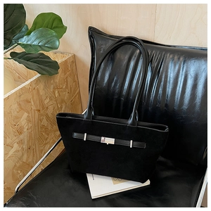Close-up of black suede tote bag with leather trim and silver buckle on a stylish bench