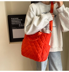 Detail of bright orange quilted nylon tote bag with wide strap and side pocket