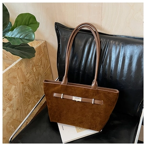 Close-up of brown suede tote bag with silver metal buckle on a black leather chair