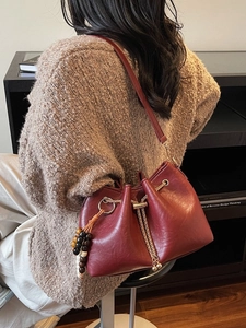 Burgundy pleated drawstring bucket bag with chain strap and tassel detail on model