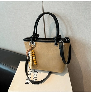Detail of khaki suede bucket bag with black leather straps and decorative wooden beads