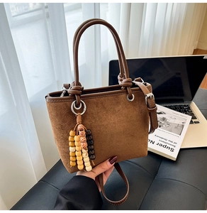 Detail view of brown suede bucket bag featuring elegant wooden bead tassel accessory