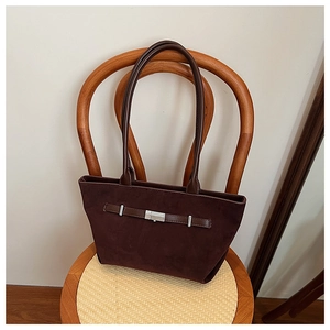Detail of dark coffee suede tote bag with silver buckle on a wooden rattan chair