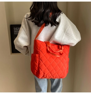 Detail of orange quilted tote bag featuring diamond pattern and wide nylon shoulder strap